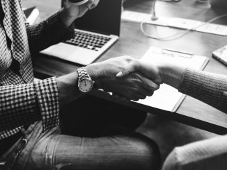 People shaking hands in front of a table with a laptop on it