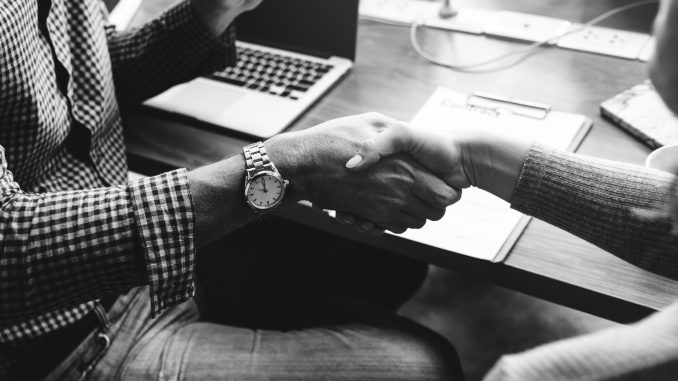 People shaking hands in front of a table with a laptop on it