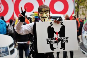 Man wearing a Guy Fawkes Mask at a protest holding a sign
